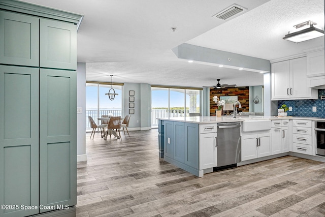8984 Puerto Del Rio Dr Unit 202, Cape Canaveral, FL 32920 - kitchen with stainless steel appliances, a peninsula, white cabinets, decorative backsplash, and light wood-style flooring