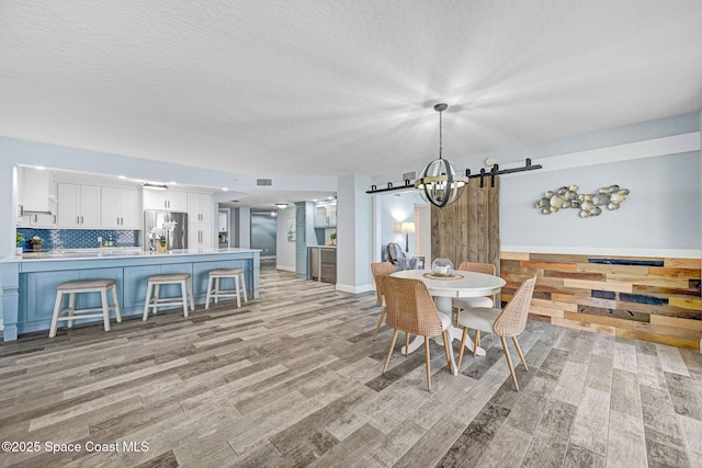 8984 Puerto Del Rio Dr Unit 202, Cape Canaveral, FL 32920 - dining area with a chandelier, light wood-style flooring, a barn door, and a textured ceiling