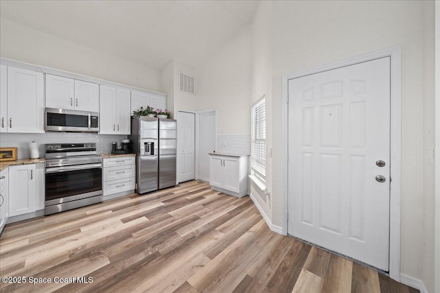 3046 Sebastian Ln, Melbourne, FL 32935 - kitchen with stainless steel appliances, high vaulted ceiling, backsplash, and white cabinetry
