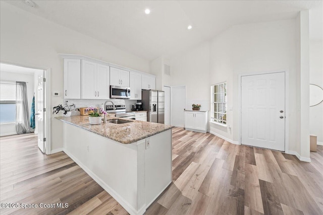 3046 Sebastian Ln, Melbourne, FL 32935 - kitchen with stainless steel appliances, high vaulted ceiling, white cabinets, a sink, and light wood finished floors