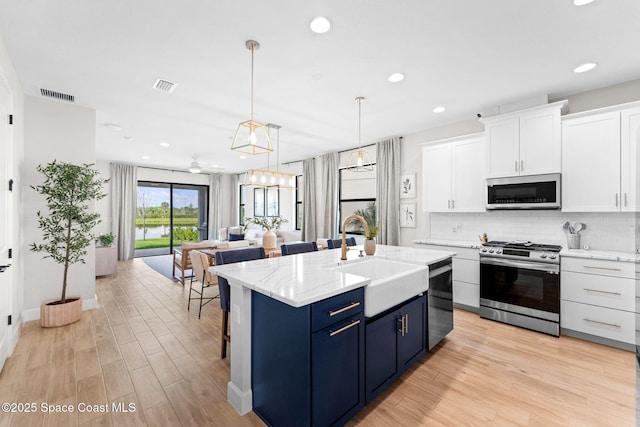 3015 Blazing Star Dr, Melbourne, FL 32940 - kitchen featuring stainless steel appliances, a sink, blue cabinetry, white cabinetry, and light wood finished floors