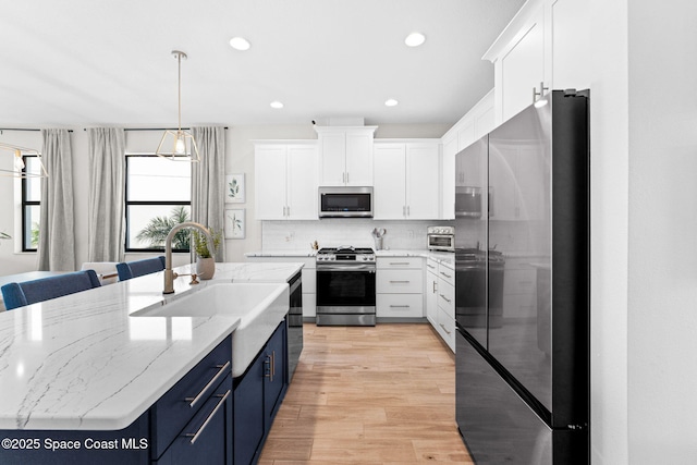 3015 Blazing Star Dr, Melbourne, FL 32940 - kitchen featuring stainless steel appliances, blue cabinets, white cabinetry, light wood-style floors, and decorative backsplash