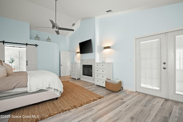 149 Kyle Ct NE, Palm Bay, FL 32907 - bedroom with light wood-type flooring, high vaulted ceiling, a barn door, a tile fireplace, and a ceiling fan