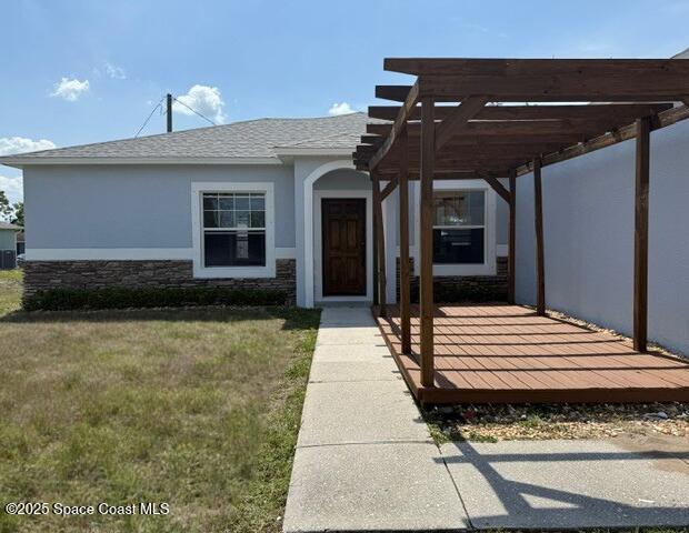 982 Colonial Ave SE, Palm Bay, FL 32909 - view of front of home with stucco siding, a pergola, a front yard, stone siding, and a shingled roof