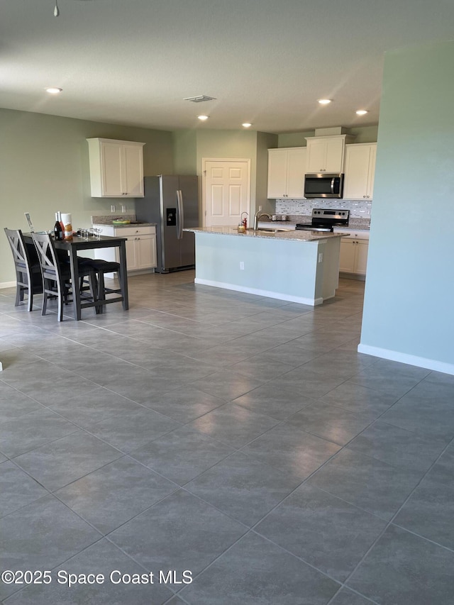 7055 Topaz Dr, Grant-Valkaria, FL 32949 - kitchen featuring stainless steel appliances, recessed lighting, tasteful backsplash, white cabinets, and a center island with sink