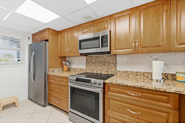 1700 N Atlantic Ave Unit 133, Cocoa Beach, FL 32931 - kitchen with stainless steel appliances, brown cabinetry, light stone countertops, backsplash, and a drop ceiling