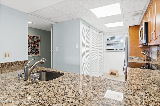 1700 N Atlantic Ave Unit 133, Cocoa Beach, FL 32931 - kitchen featuring a sink, appliances with stainless steel finishes, light stone counters, a paneled ceiling, and light tile patterned floors
