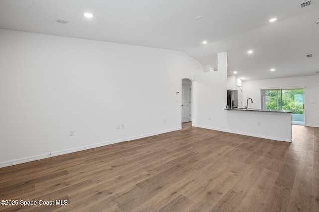 1650 Wyoming Dr SE, Palm Bay, FL 32909 - unfurnished living room featuring arched walkways, wood finished floors, lofted ceiling, a sink, and recessed lighting