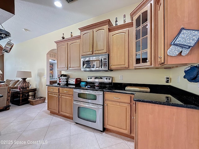 2050 SE Ellington Ter, Port St Lucie, FL 34952 - kitchen featuring stainless steel appliances, glass insert cabinets, arched walkways, light tile patterned floors, and dark stone countertops