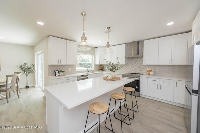 3201 Nottingham Ln, Cocoa, FL 32926 - kitchen with stainless steel appliances, wall chimney range hood, a kitchen bar, light wood-type flooring, and white cabinetry