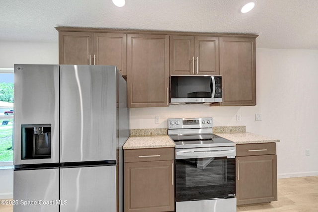 2597 Galiano Ave, Palm Bay, FL 32908 - kitchen featuring stainless steel appliances, light wood-style floors, light stone countertops, baseboards, and a textured ceiling