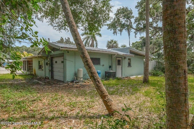 2835 Sunset Rd, Melbourne, FL 32904 - back of property featuring an attached garage, central AC unit, metal roof, and stucco siding