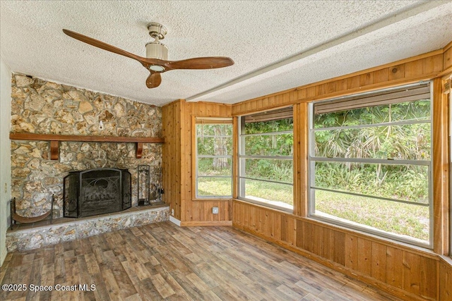 2835 Sunset Rd, Melbourne, FL 32904 - unfurnished living room with a textured ceiling, wood walls, a ceiling fan, wood finished floors, and a stone fireplace