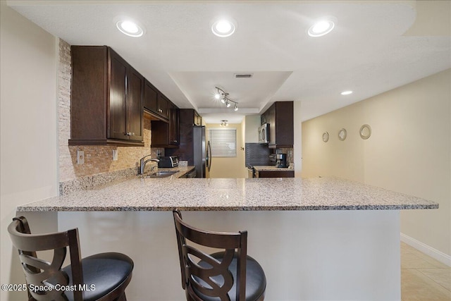 4100 Ocean Beach Blvd Unit 210, Cocoa Beach, FL 32931 - kitchen featuring a sink, appliances with stainless steel finishes, dark brown cabinetry, tasteful backsplash, and a peninsula