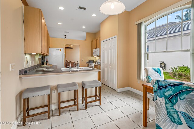 8051 Daventry Dr, Melbourne, FL 32940 - kitchen featuring white appliances, a peninsula, a breakfast bar, baseboards, and light tile patterned floors