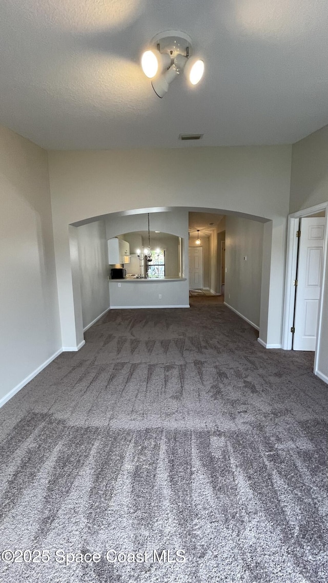 975 Luminary Cir Unit 103, Melbourne, FL 32901 - unfurnished living room featuring carpet, a chandelier, baseboards, vaulted ceiling, and a textured ceiling