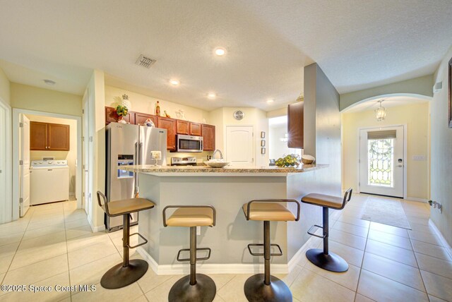 469 Aviation Ave NE, Palm Bay, FL 32907 - kitchen featuring washer / clothes dryer, stainless steel appliances, a kitchen breakfast bar, arched walkways, and light tile patterned floors