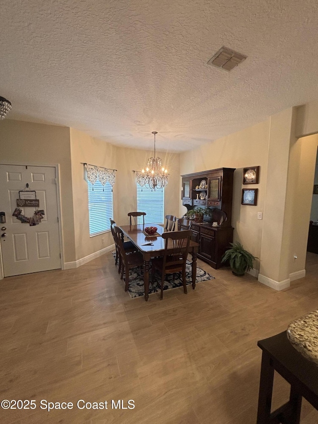 5908 Van Ness Dr, Melbourne, FL 32940 - dining space with a chandelier, a textured ceiling, baseboards, and light wood-style floors