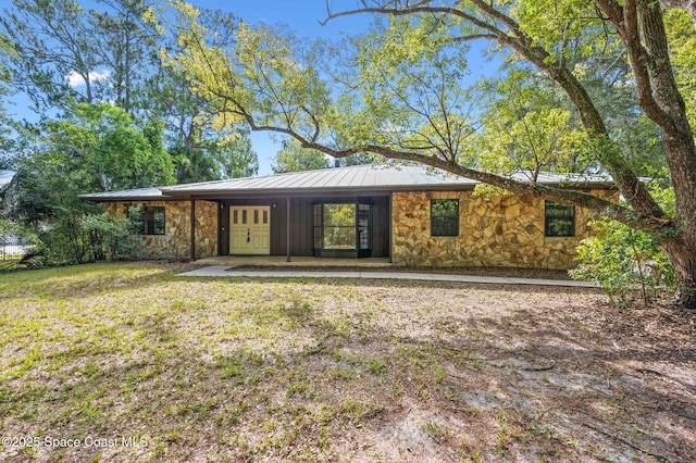 7001 Windover Way, Titusville, FL 32780 - view of front of home with stone siding, a metal roof, a front yard, and a standing seam roof