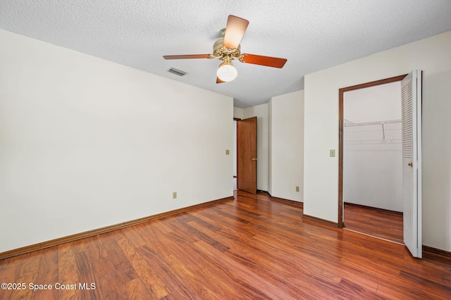 7001 Windover Way, Titusville, FL 32780 - unfurnished bedroom featuring wood finished floors, a closet, a walk in closet, a ceiling fan, and a textured ceiling