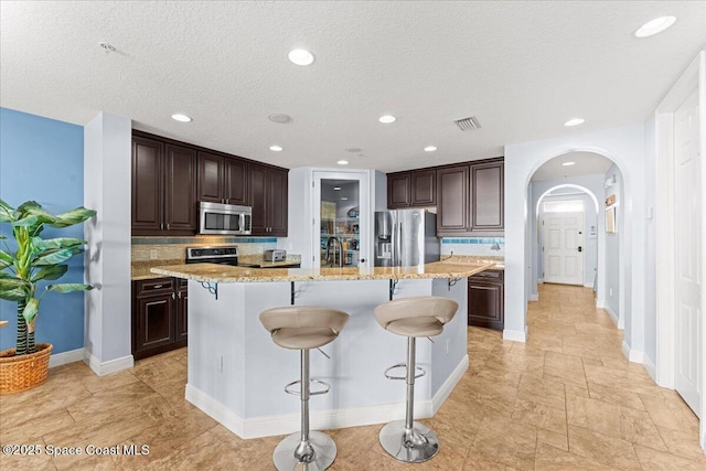 4125 W End Rd Unit 405, Cocoa Beach, FL 32931 - kitchen with stainless steel appliances, a breakfast bar, dark brown cabinets, decorative backsplash, and a textured ceiling