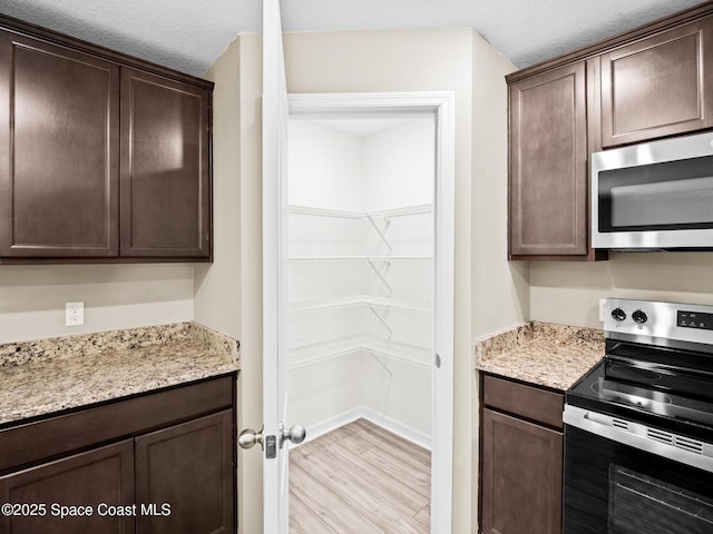 999 Zambrana St SE, Palm Bay, FL 32909 - kitchen with stainless steel appliances, dark brown cabinetry, light wood-type flooring, light stone countertops, and a textured ceiling