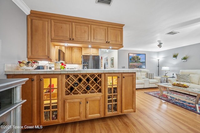 109 Plover Ln Unit 4-35, Rockledge, FL 32955 - kitchen featuring stainless steel fridge, light wood-style floors, open floor plan, brown cabinetry, and ornamental molding