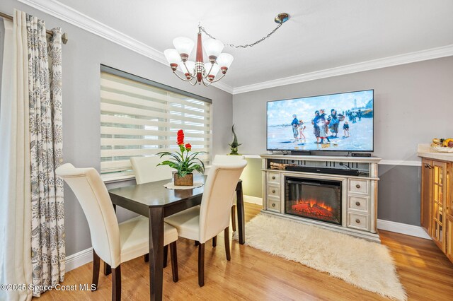 109 Plover Ln Unit 4-35, Rockledge, FL 32955 - dining space featuring a chandelier, crown molding, light wood-type flooring, a glass covered fireplace, and baseboards