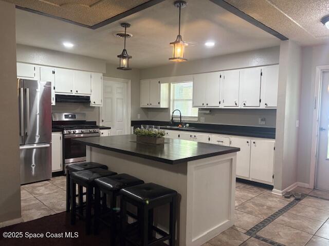 2109 Ivy Dr, Cocoa, FL 32922 - kitchen with appliances with stainless steel finishes, dark countertops, range hood, white cabinets, and light tile patterned floors