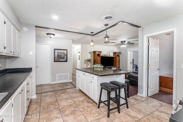 2109 Ivy Dr, Cocoa, FL 32922 - kitchen with dark countertops, white cabinetry, a breakfast bar, ceiling fan, and decorative light fixtures