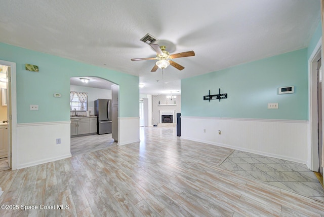 581 Howe Ave SE, Palm Bay, FL 32909 - unfurnished living room with ceiling fan, a wainscoted wall, light wood-type flooring, a fireplace, and arched walkways