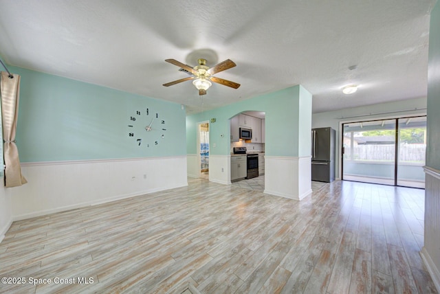 581 Howe Ave SE, Palm Bay, FL 32909 - unfurnished living room with arched walkways, light wood finished floors, a wainscoted wall, ceiling fan, and a textured ceiling