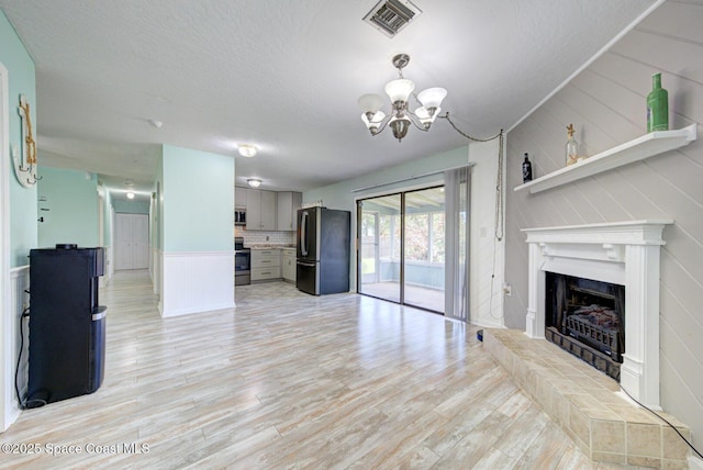 581 Howe Ave SE, Palm Bay, FL 32909 - unfurnished living room with a chandelier, light wood-style flooring, a fireplace, a decorative wall, and a textured ceiling