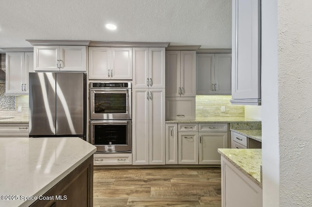 3221 S Atlantic Ave Unit 703, Cocoa Beach, FL 32931 - kitchen with appliances with stainless steel finishes, decorative backsplash, light wood finished floors, a textured ceiling, and light stone countertops