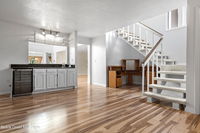 105 Osprey Ct, Melbourne, FL 32940 - unfurnished living room featuring beverage cooler, light wood-style floors, stairs, a textured ceiling, and baseboards