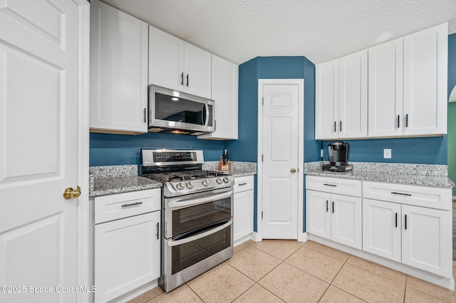 5256 Mansford Pl, Melbourne, FL 32940 - kitchen featuring appliances with stainless steel finishes, white cabinets, light tile patterned floors, light stone counters, and a textured ceiling