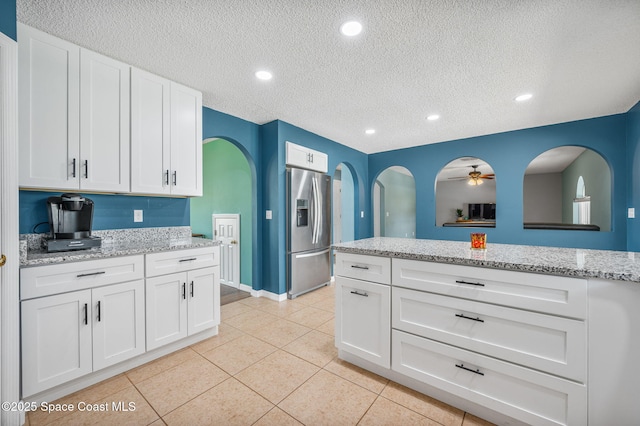 5256 Mansford Pl, Melbourne, FL 32940 - kitchen featuring stainless steel fridge, a textured ceiling, white cabinetry, light tile patterned flooring, and light stone countertops