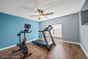 5256 Mansford Pl, Melbourne, FL 32940 - workout area featuring a textured ceiling, baseboards, ceiling fan, and wood finished floors