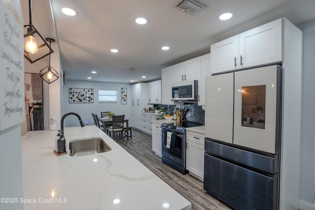 629 Tupelo Dr, Melbourne, FL 32935 - kitchen featuring appliances with stainless steel finishes, a sink, white cabinets, wood finished floors, and light stone counters