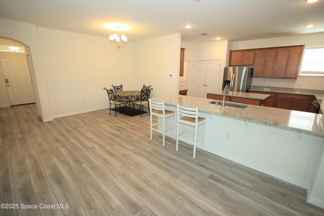 8342 Laguna Cir, Micco, FL 32976 - kitchen with a sink, stainless steel fridge, a breakfast bar area, brown cabinetry, and light wood-style floors