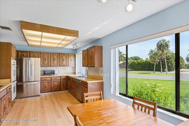 1181 Fairway Ct NE, Palm Bay, FL 32905 - kitchen featuring appliances with stainless steel finishes, light wood-type flooring, brown cabinets, decorative backsplash, and a textured ceiling