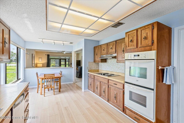 1181 Fairway Ct NE, Palm Bay, FL 32905 - kitchen with double oven, under cabinet range hood, brown cabinetry, backsplash, and light countertops