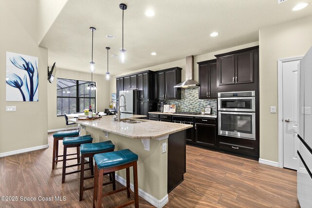 7914 Creshire Ct, Melbourne, FL 32940 - kitchen featuring wall chimney exhaust hood, a kitchen island with sink, appliances with stainless steel finishes, baseboards, and a breakfast bar