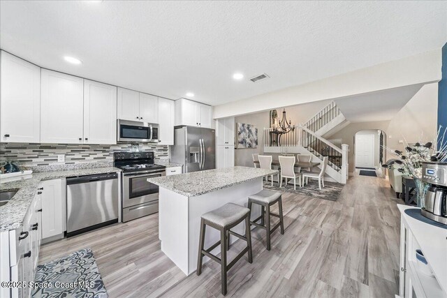 977 Osprey Dr, Melbourne, FL 32940 - kitchen featuring stainless steel appliances, arched walkways, a breakfast bar area, light wood finished floors, and decorative backsplash