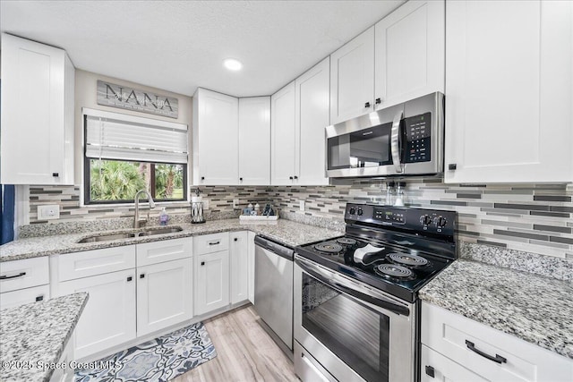 977 Osprey Dr, Melbourne, FL 32940 - kitchen with appliances with stainless steel finishes, a sink, light wood finished floors, white cabinets, and a textured ceiling