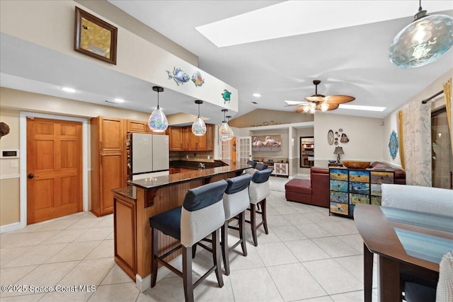 1510 Jupiter Blvd NW, Palm Bay, FL 32907 - kitchen featuring freestanding refrigerator, a kitchen breakfast bar, brown cabinets, a skylight, and light tile patterned floors