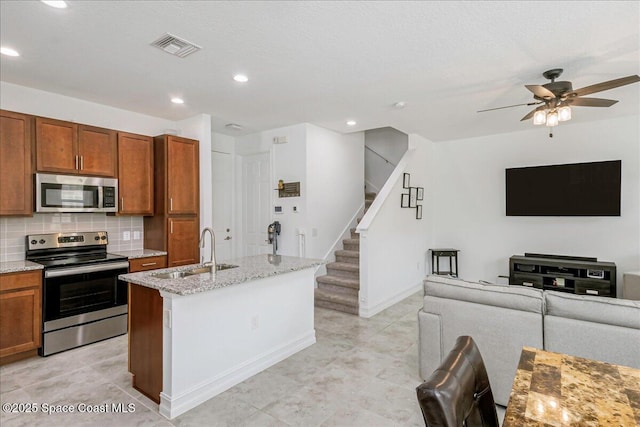1475 Isabella Dr Unit 101, Melbourne, FL 32935 - kitchen featuring appliances with stainless steel finishes, brown cabinetry, open floor plan, decorative backsplash, and light stone counters