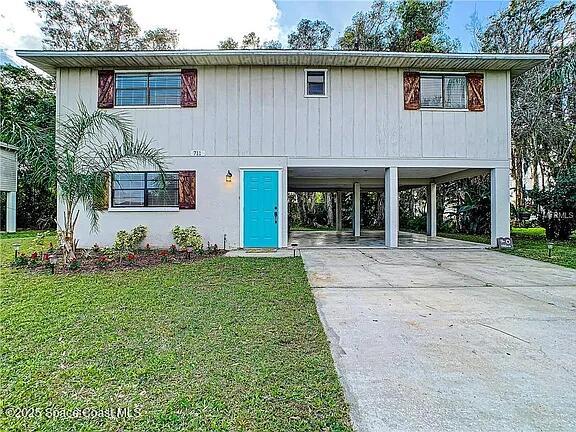 711 47th St W, Palmetto, FL 34221 - raised beach house featuring concrete driveway, a front lawn, and a carport