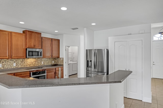 310 Chennault Ln, Rockledge, FL 32955 - kitchen featuring stainless steel appliances, washing machine and clothes dryer, light tile patterned flooring, decorative backsplash, and brown cabinetry