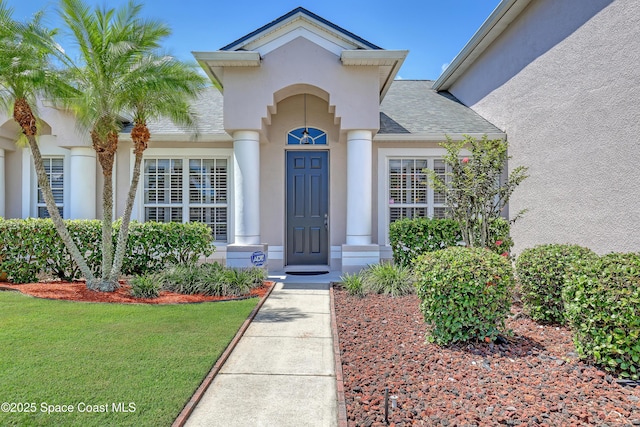 310 Chennault Ln, Rockledge, FL 32955 - view of exterior entry featuring stucco siding, roof with shingles, and a yard